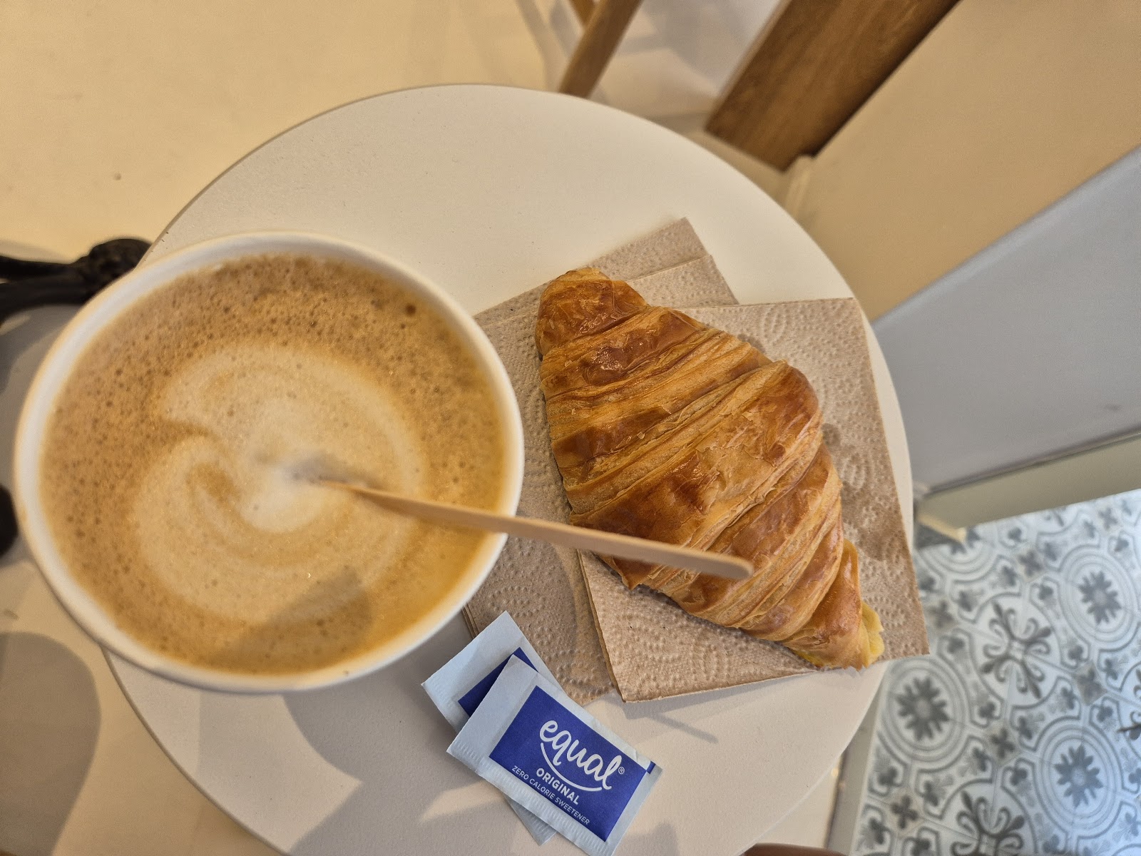Cappuccino and a butter croissant on a marble bistro table over patterned Punda tiles
