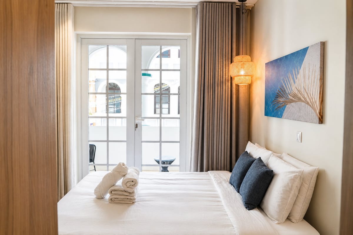 The king bed with the balcony doors beside it, the white arcade and a painted facade framed in the glass