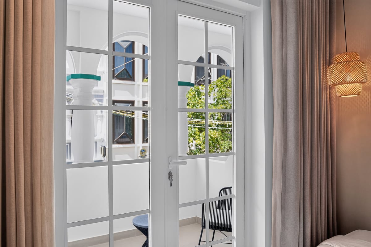 The French doors of a balcony room at Majestic City Palace standing open onto the loggia, with a bistro table and chair on the tiled floor outside