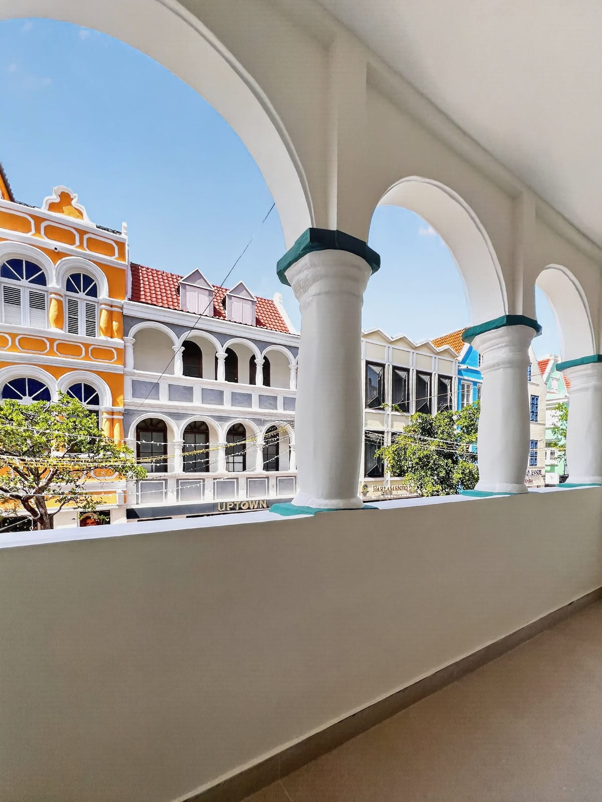 The view from the upstairs loggia of Majestic City Palace through a white arch, onto the painted Dutch colonial merchant houses of Breedestraat in Punda