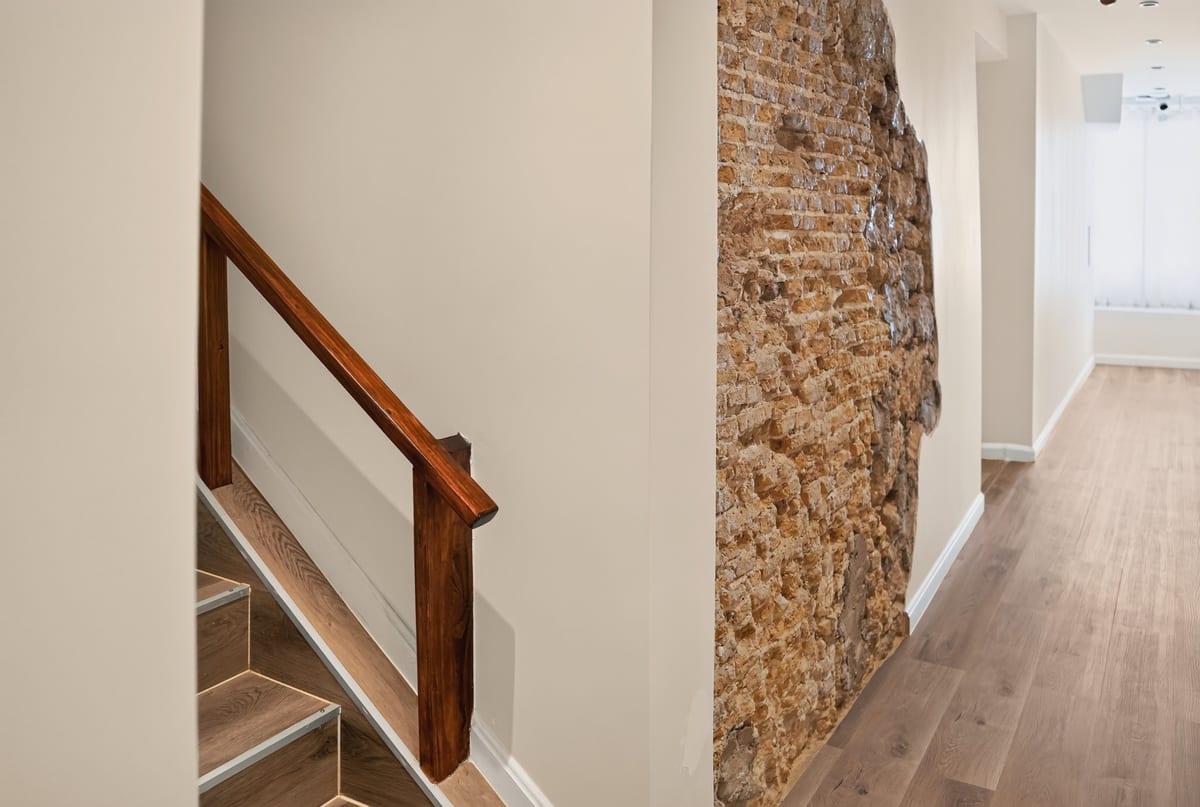 The staircase at Majestic City Palace with a dark wood handrail, plain plaster walls and a panel of exposed coral stone on the landing