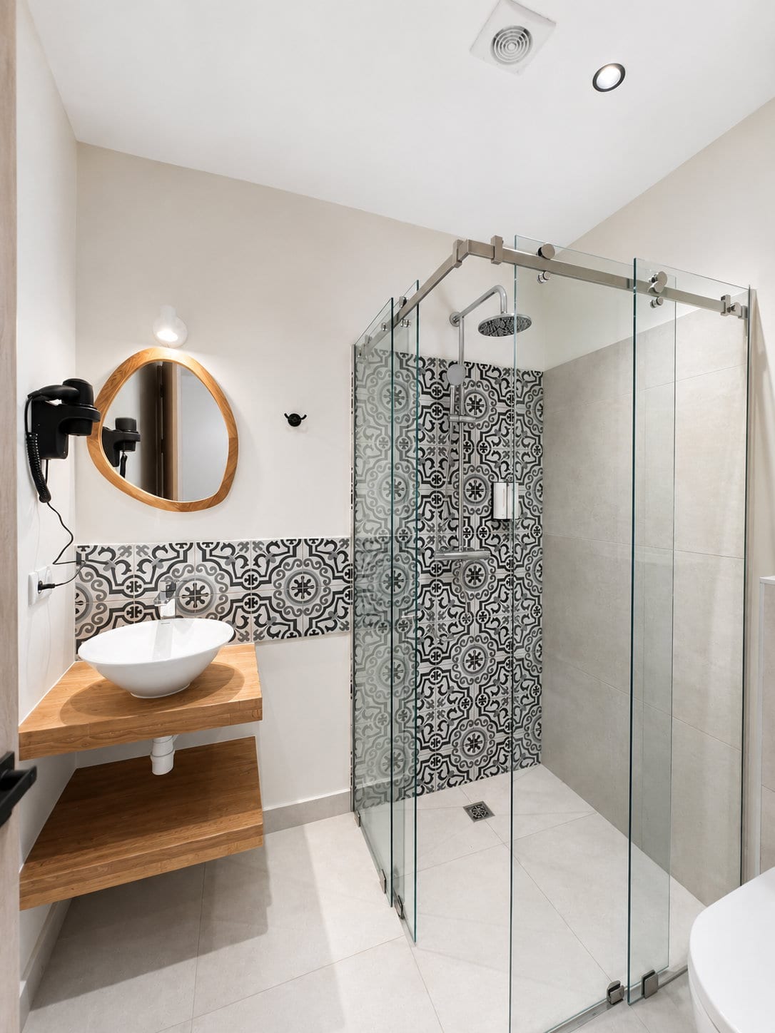 A Signature King Room bathroom with a vessel basin on an oak shelf, an arched mirror, a band of majolica along the wall and a glass walk in shower