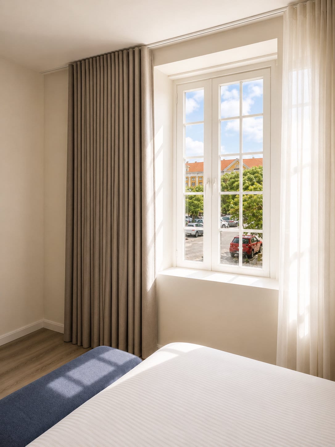 A tall second floor casement window looking onto the trees, the street and the tiled roofs of Punda, with long drapes and a sheer curtain either side