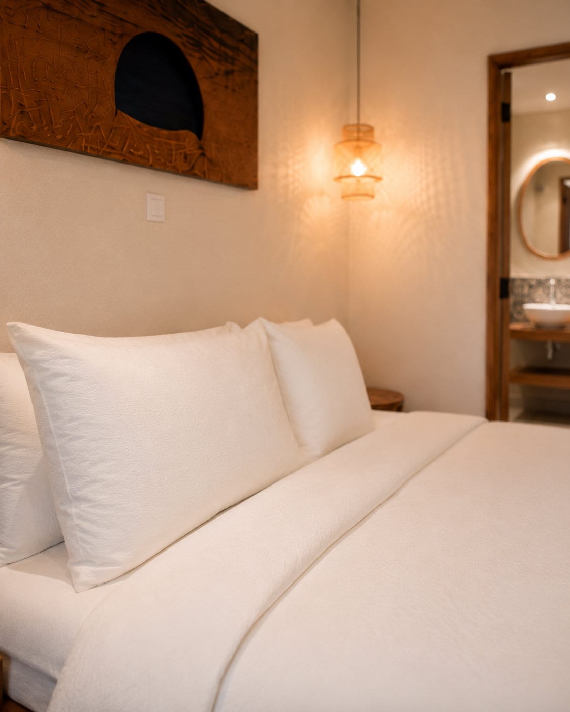 Pillows in white linen close up, with a carved canvas above the bed and the basin and arched mirror beyond the door
