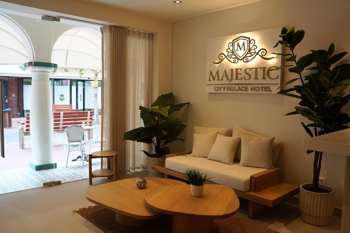 The lobby sofa and low oak tables, with the hotel crest lit on the wall and the arcade visible through the glass