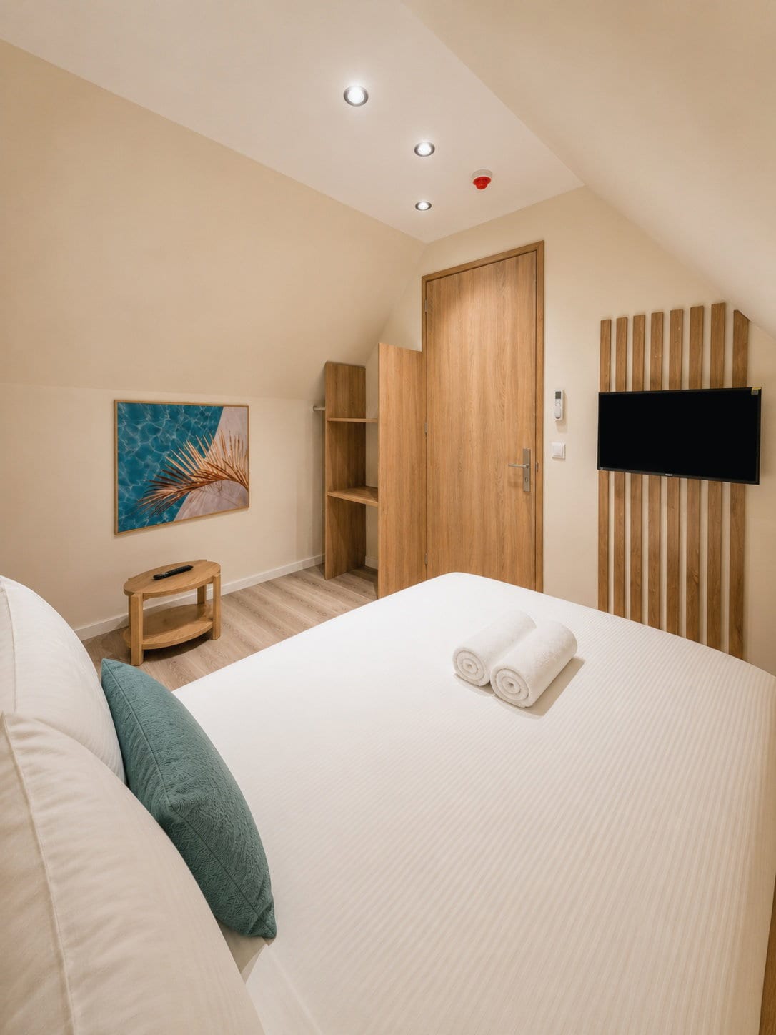 The bed with a teal cushion in the foreground, a painted canvas on the wall, the oak entrance door and the slatted television wall beyond