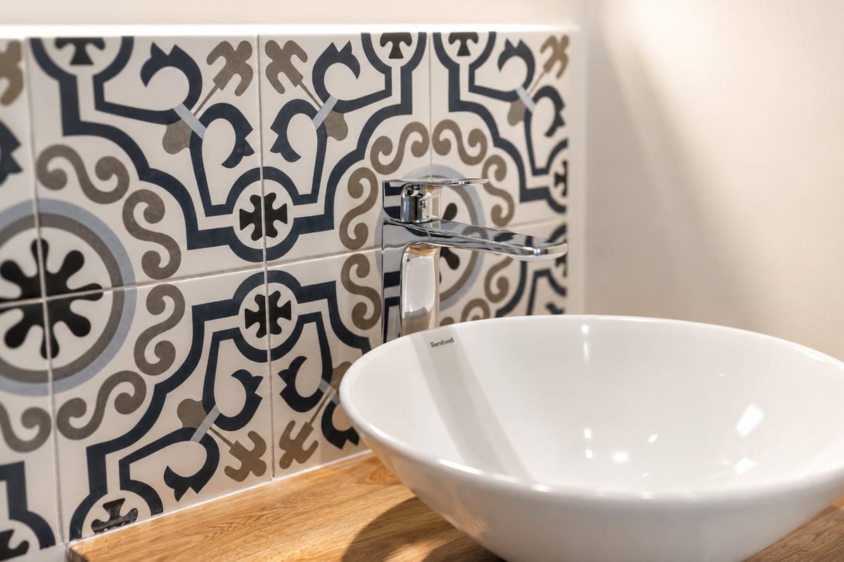 A white vessel basin on an oak shelf in front of a wall of blue and white patterned majolica tile in a bathroom at Majestic City Palace