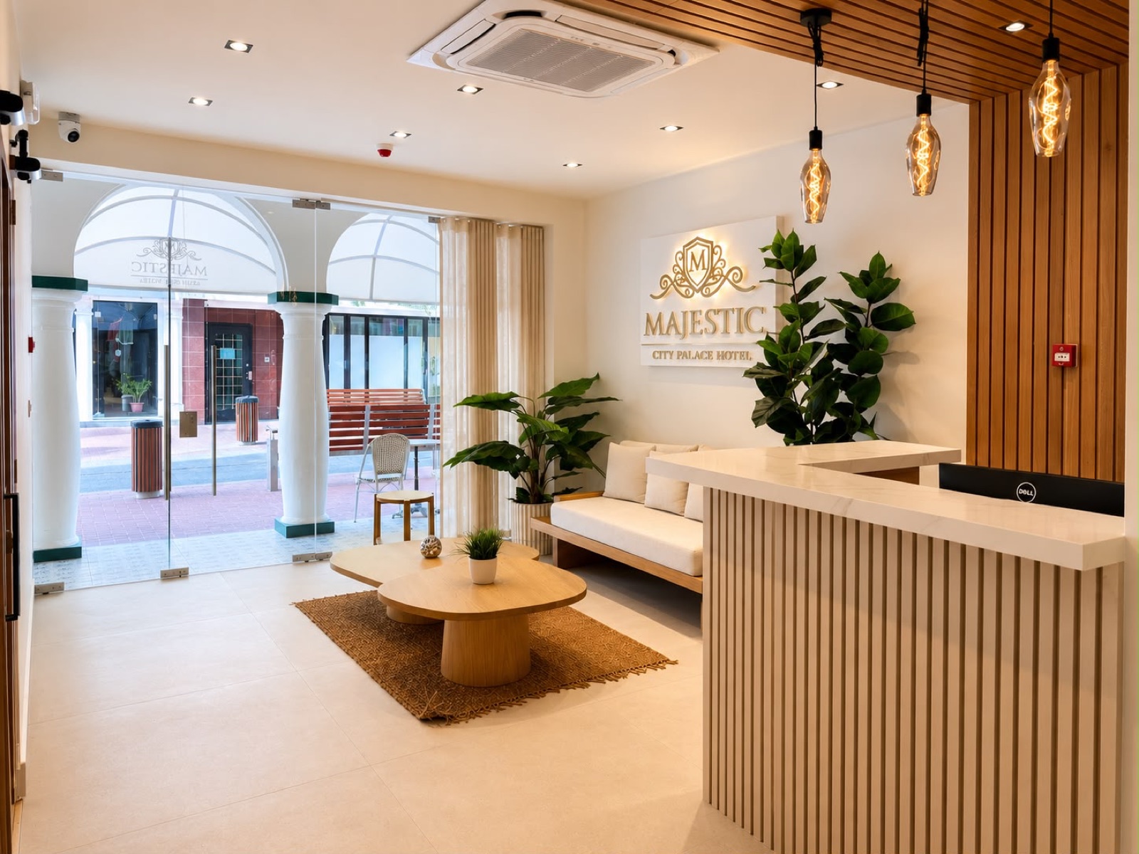 Majestic City Palace reception, fluted white desk under a slatted walnut ceiling, filament pendants, the gold crest glowing on the wall and the arcade beyond the glass