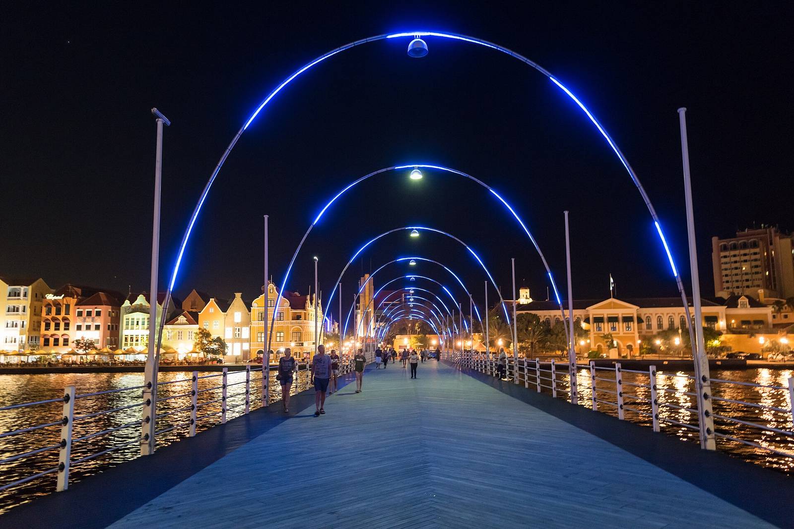 The illuminated arcs of the Queen Emma Bridge glowing over the harbor at night in Willemstad